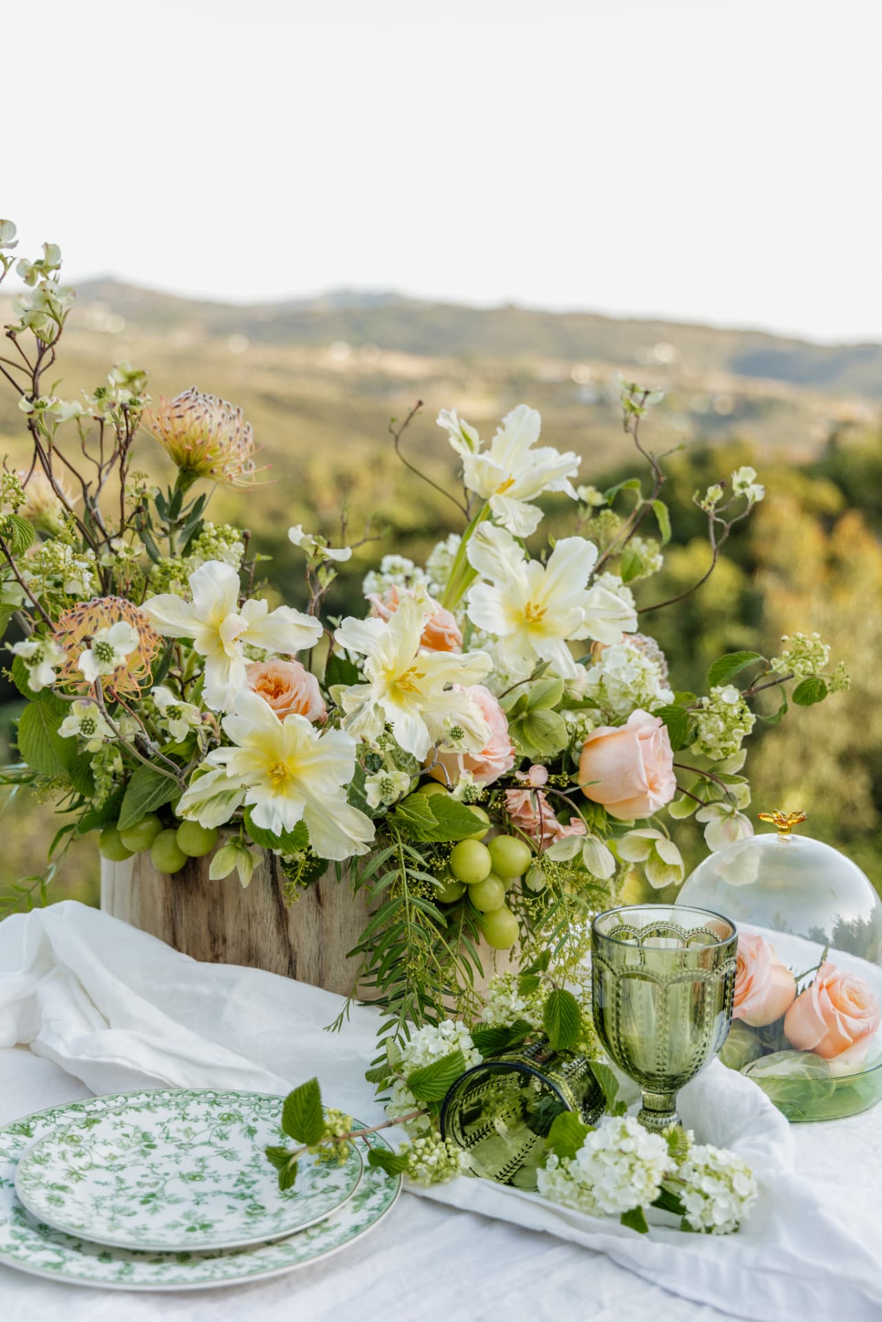 White and peach flowers with green goblets on a hillside table